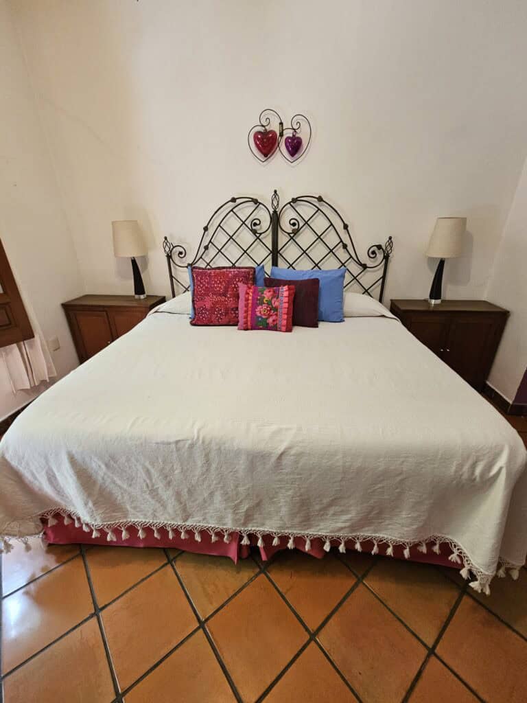 Room view at La Casa de Mis Recuerdos B&B in Oaxaca, Mexico - a black metal bed with red, pink and blue pillows
