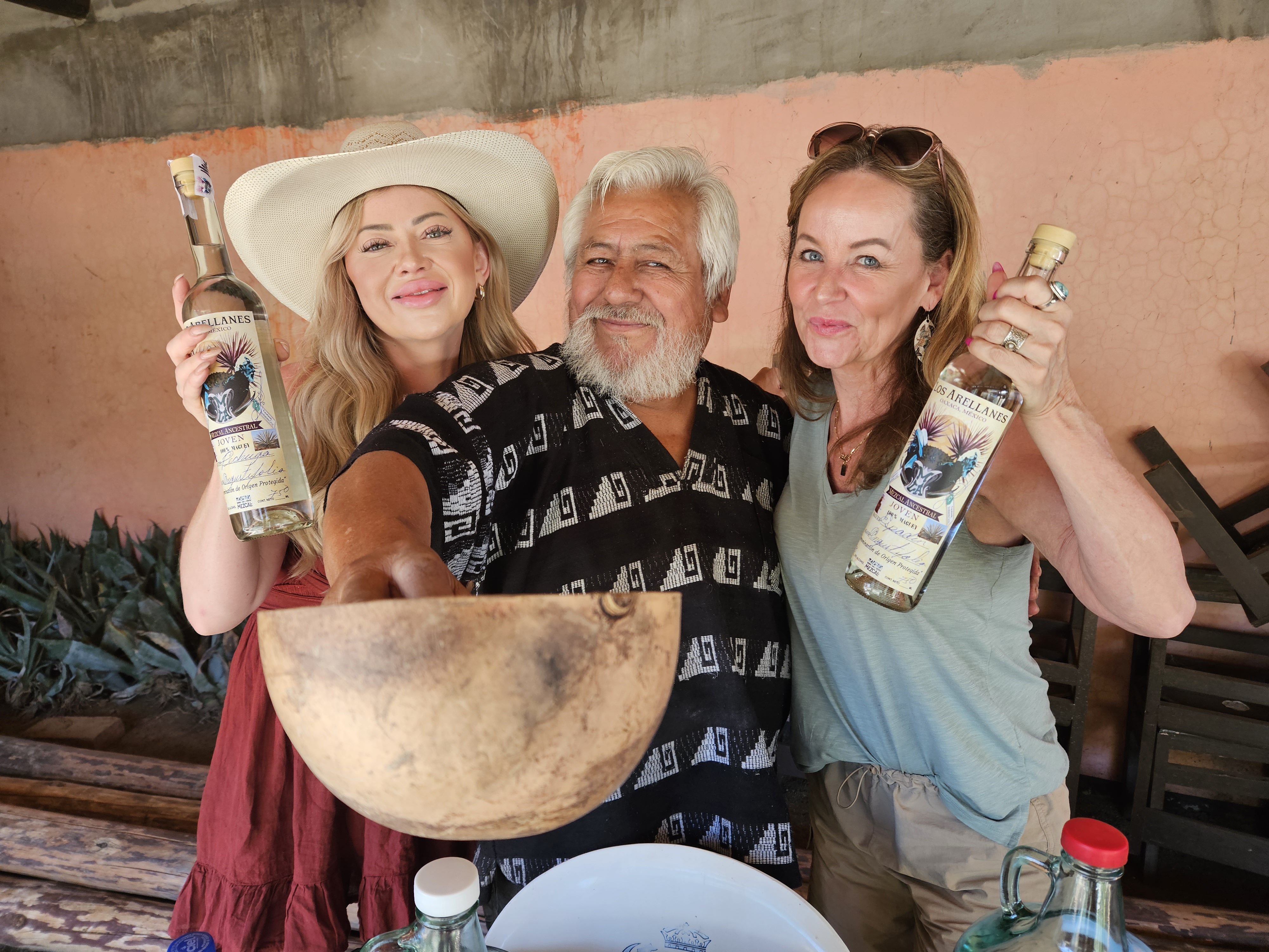 Photo of me, owner of the palengue (place where Mezcal is made) and another traveler holdingup bottles of Mezcal in Oaxaca Mexico