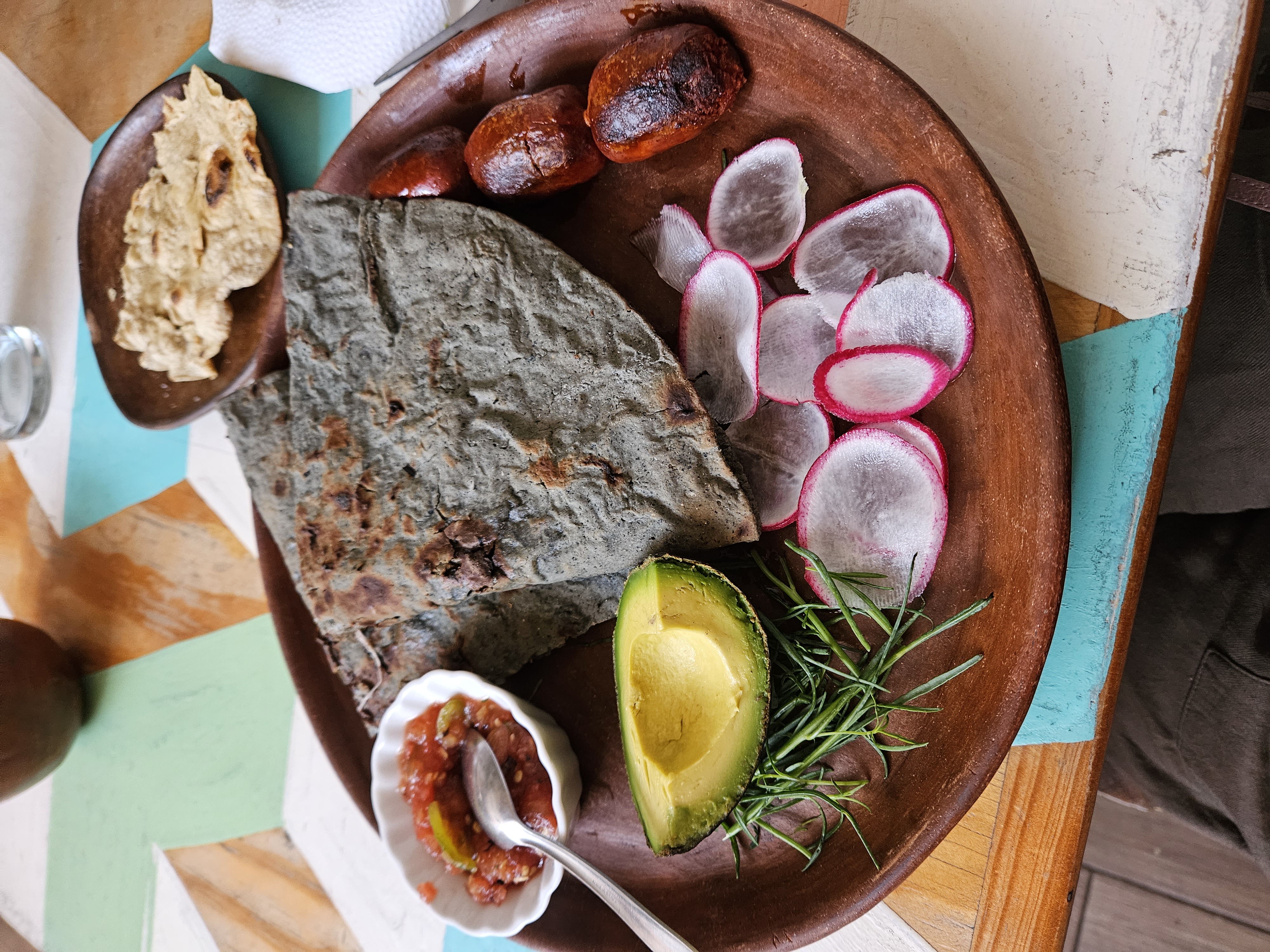 A dish of food with a tlayuda (crispy corn tortilla) with a side of avocado, radishes and tomatoes in Oaxaca Mexico