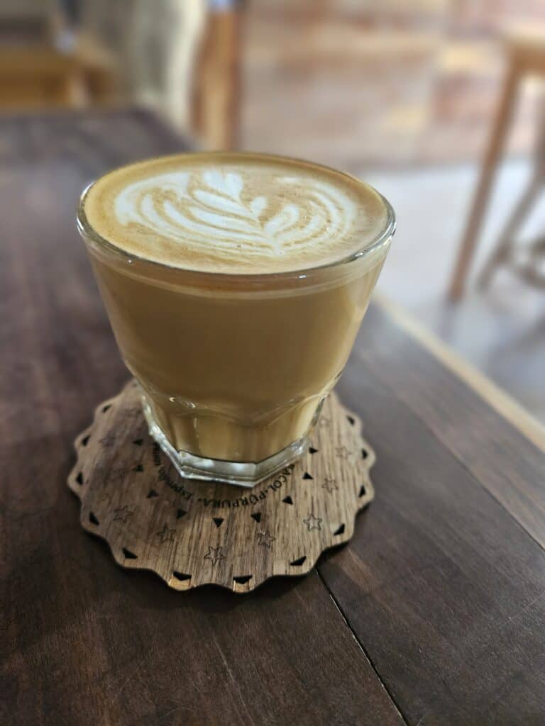 A clear glass of cappuccino with heart designs in the foam
