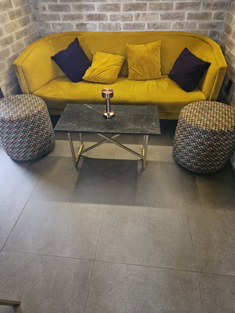 Beautiful seating area with yellow gold sofa, black pillows, puffs and coffee table inside of La Petrona restaurant in Oaxaca