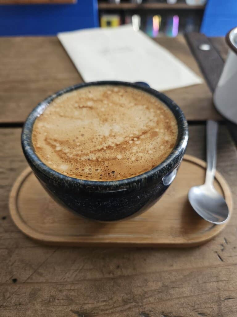 Cappuccino in a blue coffee mug placed on a wooden tray with a silver spoon