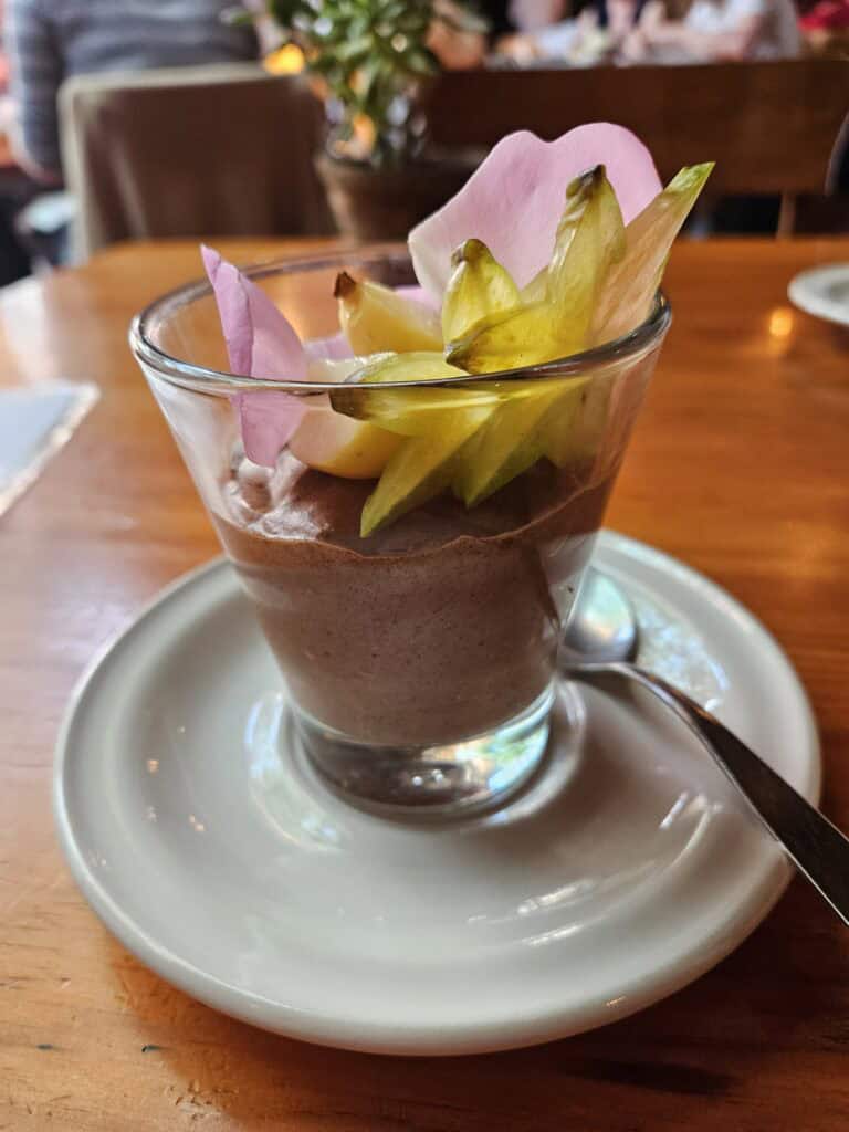 A glass filled with a chocolate mousse with decorate yellow and pink flowers.