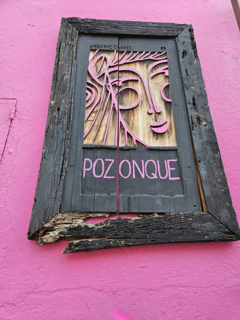 Black wooden sign with pink lettering and a woman's face in a carved relief advertising Pozonque Café in Oaxaca Mexico