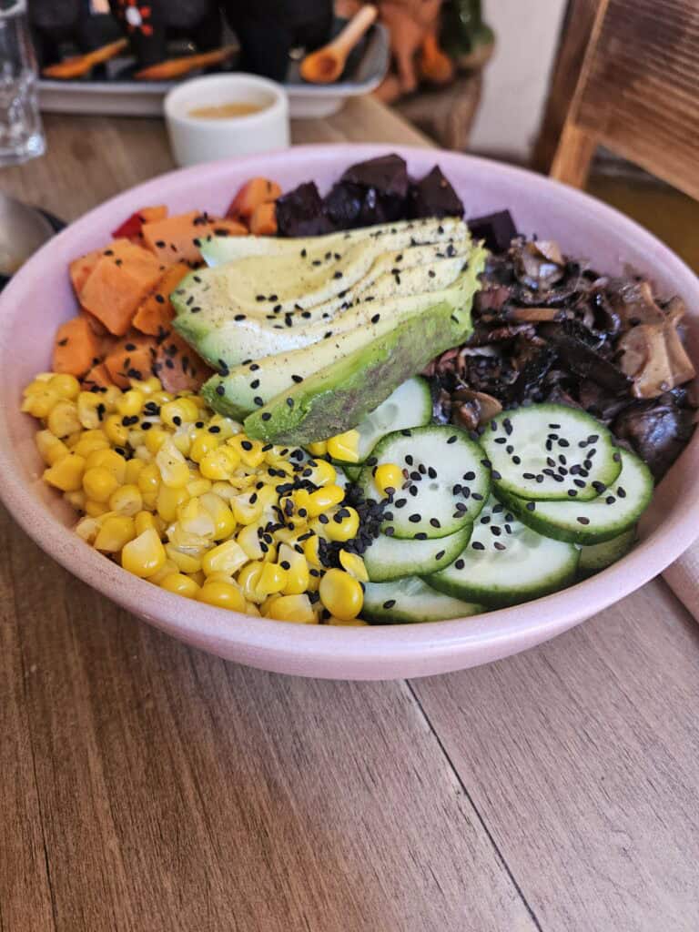 Pink bowl with vegetables including avocado, corn, carrots, beets, cucumbers and rice