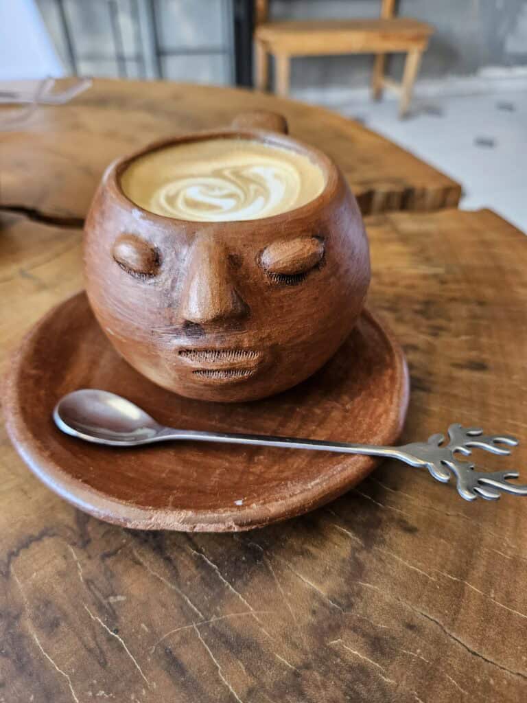 terra cotta cup filled with coffee with a face sculpted as part of the design on a matching plate with a silver spoon.