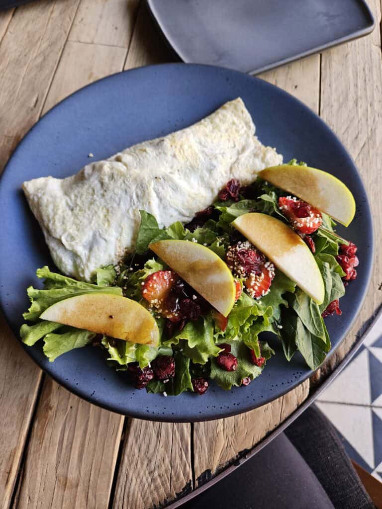 Omelet and salad with apples, berries and a blaze on a blue plate