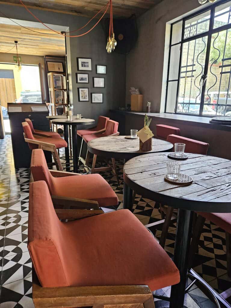 Interior of Expendio Tradición, restaurant in Oaxaca, Mexico. Pumpkin orange chairs around round, wooden tables with the the light streaming in from outside.