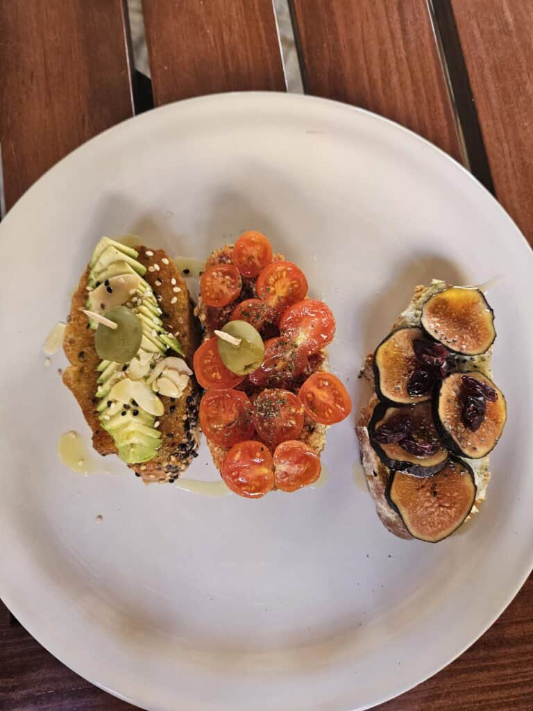 White plate with three small appetizers or tapas with avocado, tomatoes and fruit