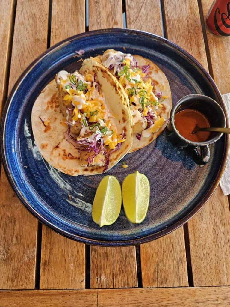 Two fish tacos with a side of salsa and lime slices on a blue plate