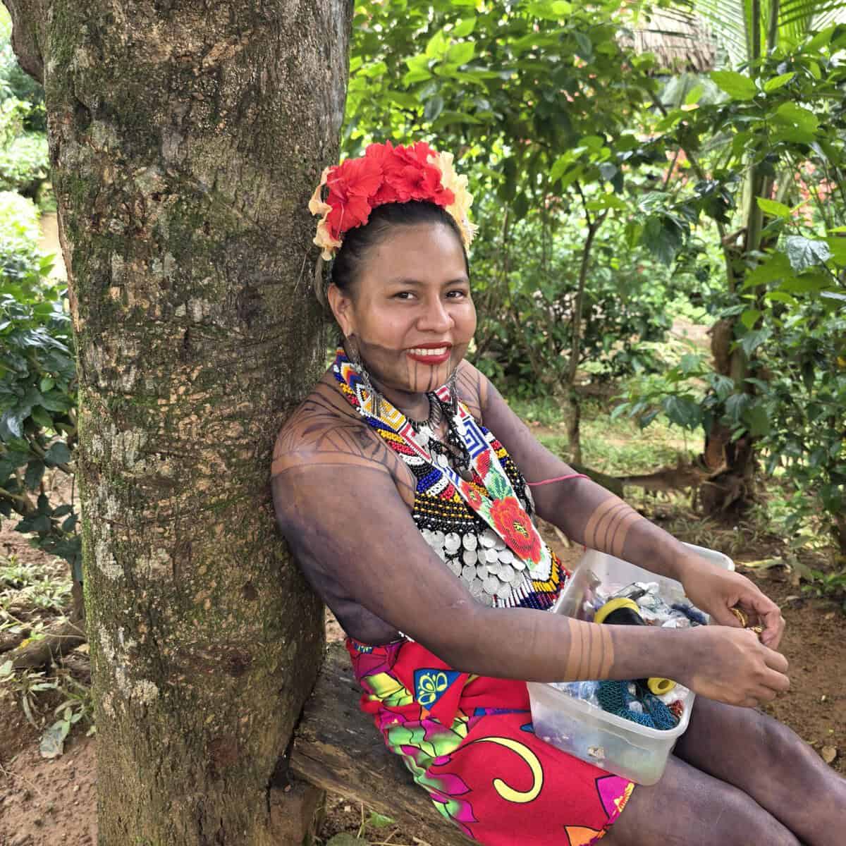 Beautiful Embera woman in her village sitting against a tree.