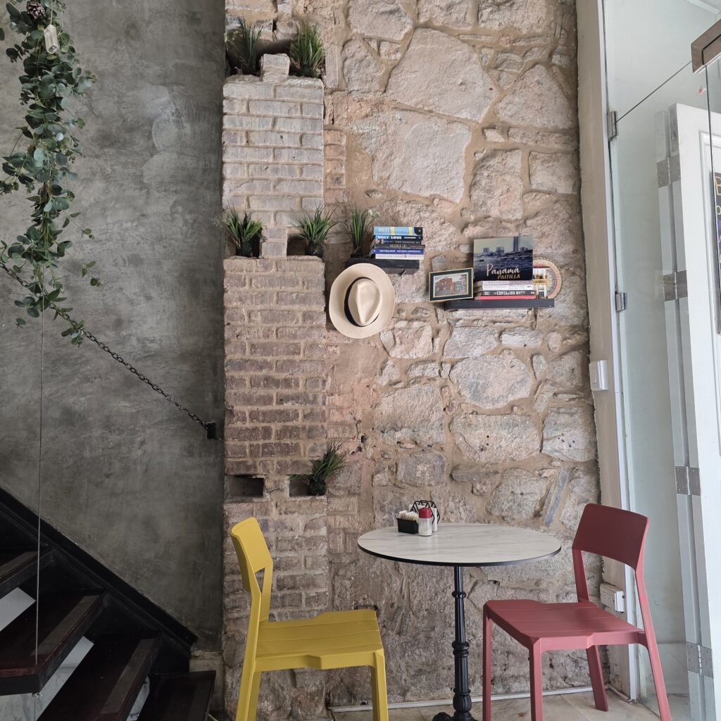 Stone wall and a table with a yellow and red chair inside Morah Cafe in Casco Viejo Panama