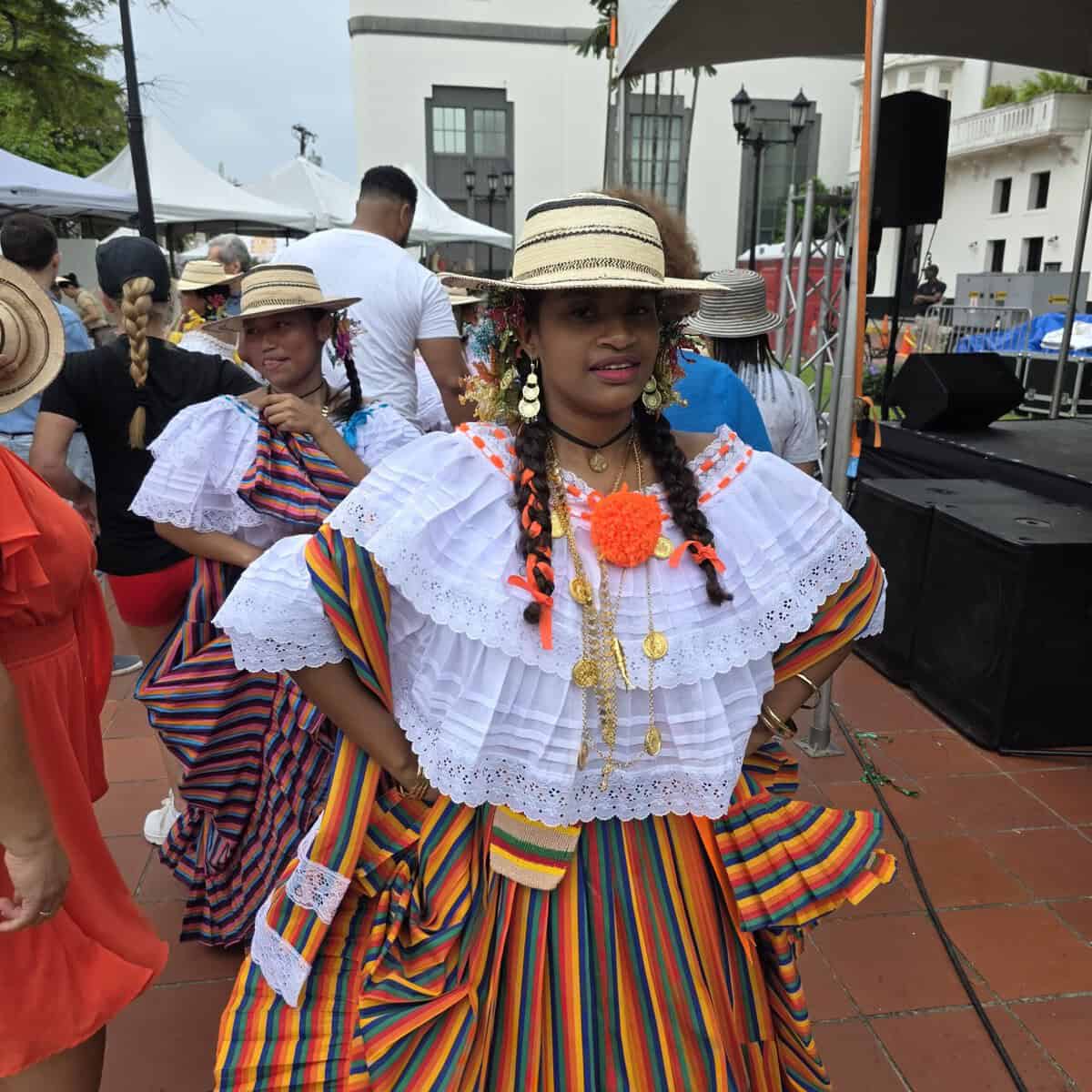 Young girl wearing traditional clothing in a square in Panama City. Her hair is in braids, her blouse is white and her skirt is multi colored organge, yellow, blue and teal.