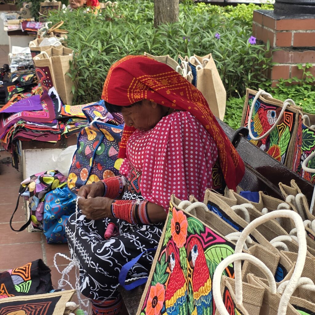 Kuna woman of Panama dressed in a red scarf, red and white check blouse as she creates traditional art