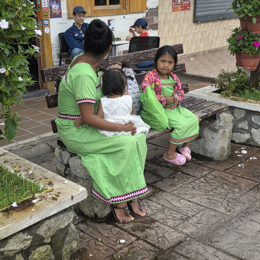 A woman, and two little girls dressed traditionally in green dresses with color trim sitting on a stone bench in Boquete in Panama