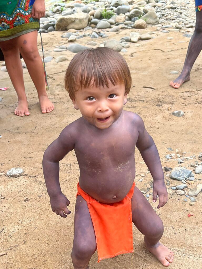 Small child in Embera village in Panama. He has on a reddish-orange skirt and has a mischievous look on his face.